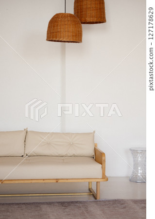 Beige wooden sofa and wicker lamps in minimal studio interior with white wall and copy space 127178629