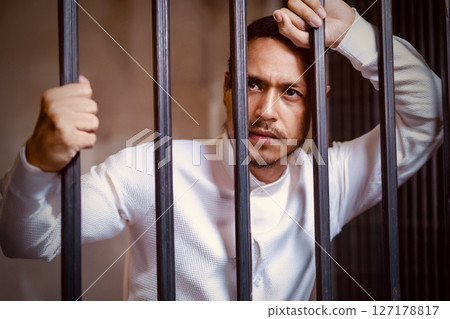 A man in white clothes is protesting his innocence from behind iron bars 127178817