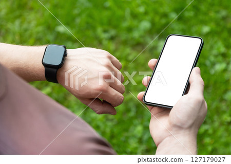 Close up man hands checking his heartbeat with smartwatch and mobile phone at nature park. Male checking pulse after jogging. Fitness tracker. Mock up. Space for design Close up man hands checking his heartbeat with smartwatch and mobile phone at nature park. Male checking pulse after jogging. Fitness tracker. Mock up. Space for design 127179027