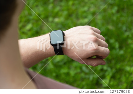 Close up man hands checking his heartbeat with smartwatch at nature park. Male checking pulse after jogging. Fitness tracker 127179028