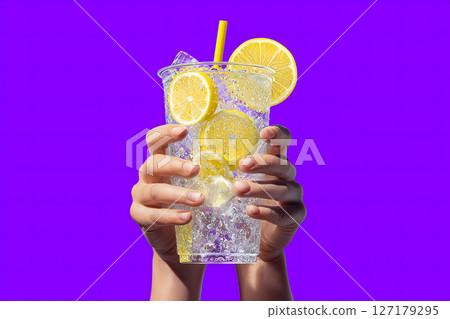 Refreshing drink with lemon slices in clear cup, held by hands against vibrant purple background, evokes sense of summer joy 127179295