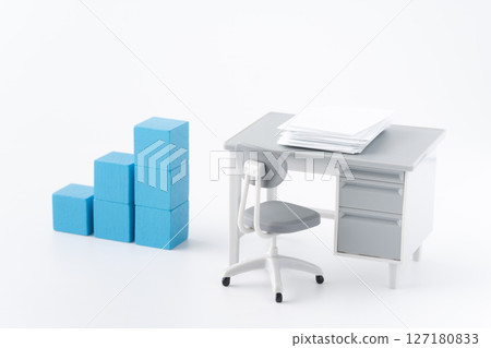 A miniature office desk with documents and blue building blocks arranged in a staircase 127180833