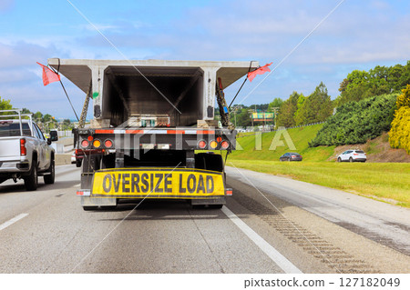 Large truck equipped with an oversize load sign drives along busy highway under transportation in motion. Large truck equipped with an oversize load sign drives along busy highway under transportation in motion. 127182049