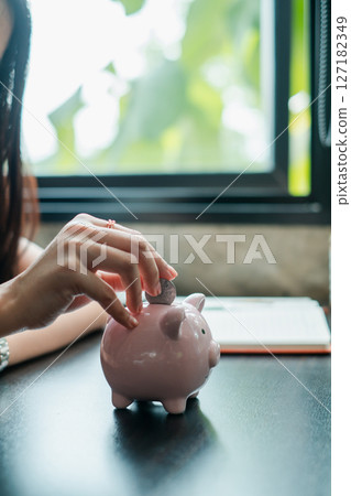 Close-up of a hand inserting a coin into a pink piggy bank, symbolizing savings and financial planning. 127182349
