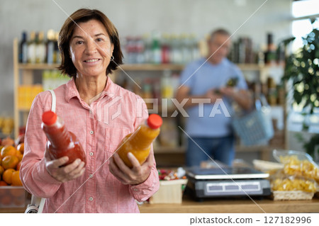 Elderly woman chooses peach and tomato juice Elderly woman chooses peach and tomato juice 127182996