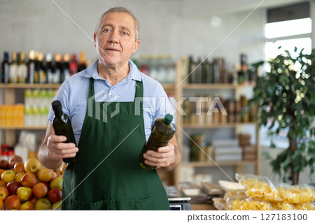 Elderly man seller offers olive oil in grocery store 127183100