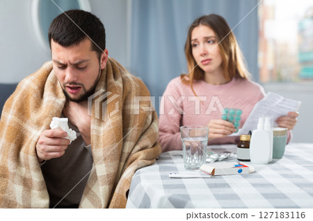 Ill man sitting at table near his wife who helping him with medicine Ill man sitting at table near his wife who helping him with medicine 127183116