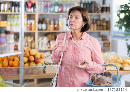 Mature woman choosing something in grocery store Mature woman choosing something in grocery store 127183134