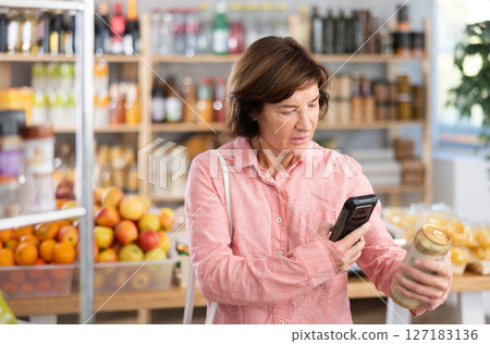 Mature woman is scanning QR on a can of beer in grocery Mature woman is scanning QR on a can of beer in grocery 127183136