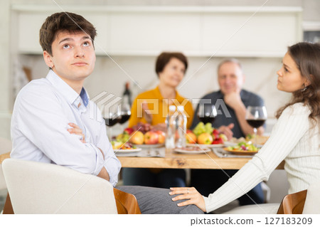 Dissatisfied guy turned away from the festive table, where his family and friends were having conversation. Quarrel during home dinner Dissatisfied guy turned away from the festive table, where his family and friends were having conversation. Quarrel during home dinner 127183209