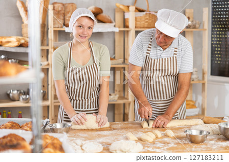 Experienced elderly baker and young girl knead the dough together and cut raw dough with knife 127183211