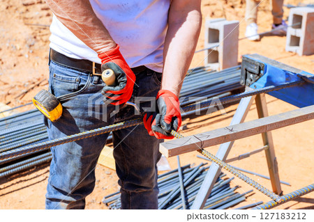 Construction worker grips metal rebar cuts while wearing gloves on busy building site. 127183212
