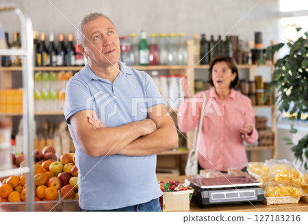 Senior wife stands behind pensioner husband and yells at companion. Senior wife stands behind pensioner husband and yells at companion. 127183216