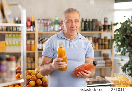 Mature man hold white plastic bottles and choose consider juice in store Mature man hold white plastic bottles and choose consider juice in store 127183344
