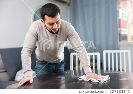 Bearded guy wiping dust on table in dining room 127183345