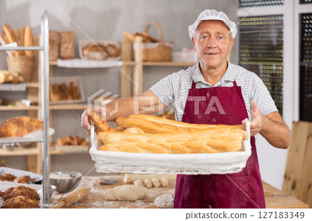 Bakery mature man employee holds basket of ready-made baguettes. 127183349
