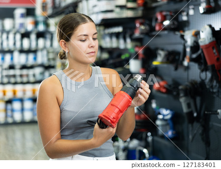 Beautiful young woman chooses and buys industrial hair dryer in hardware store Beautiful young woman chooses and buys industrial hair dryer in hardware store 127183401
