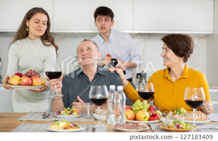 Father and mother together with adult children talking at dinner table at home 127183409