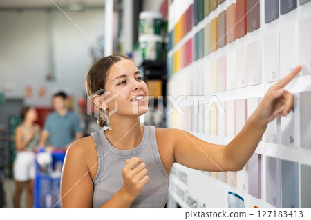 Near stand with samples paint, palette of colors of coating, woman buyer examines showcase in store 127183413