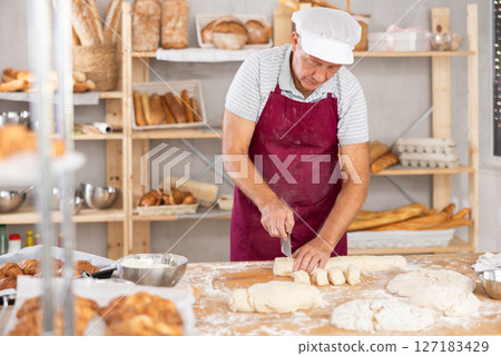 Elderly male baker cutting dough with scraper 127183429