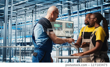 Experienced team leader doing induction to new trainees in industry 4.0 photovoltaics plant. Senior engineer in smart solar panels factory teaching interns to maximize power generation, camera A 127183473