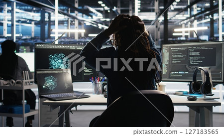 Angry server hub developer frustrated by slow data analytics AI generator. Annoyed data center worker punching desk, irked by glitching artificial intelligence program showing system metrics, camera A 127183565