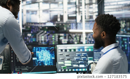 Pleased data center manager praising work done by engineer using neural network models to configure hardware. Supervisor congratulating employee for successfully using AI to optimize system, camera B 127183575