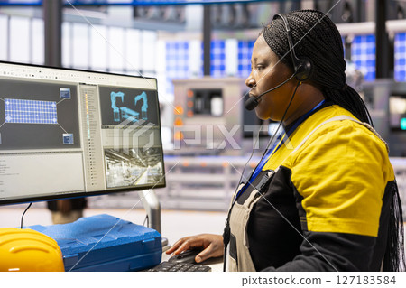 African american technician monitors automated factory conveyor belt and robotic arms, ensuring precision in industrial plant. Professional engineer uses computer in manufacturing solar panels. African american technician monitors automated factory conveyor belt and robotic arms, ensuring precision in industrial plant. Professional engineer uses computer in manufacturing solar panels. 127183584