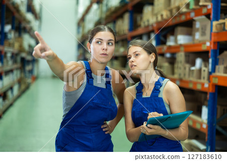 Two female storekeepers working in building store discussing important work issues in warehouse, holding paper estimate in their hands 127183610