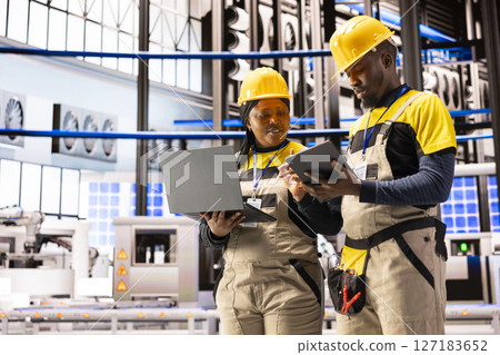 Engineers using digital interfaces on laptop and tablet to monitor and enhance efficiency in automated factory. Industry 4.0 innovation powers industrial automation in smart manufacturing facility. 127183652