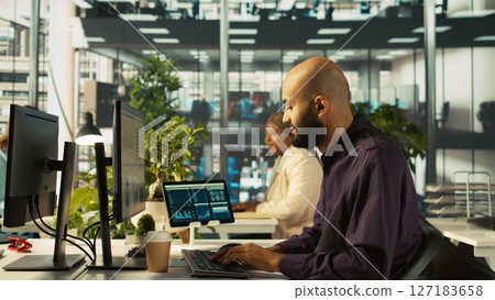 Accountant in busy workplace talking with colleagues while inputting financial figures on PC. Employee working in modern office chatting with coworkers while crosschecking data, camera B Accountant in busy workplace talking with colleagues while inputting financial figures on PC. Employee working in modern office chatting with coworkers while crosschecking data, camera B 127183658