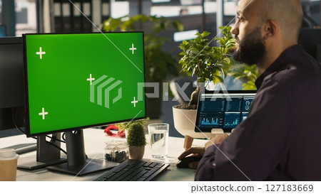 Man in office reviewing financial graphs on green screen PC, analyzing key performance indicators. Employee looking over data trends and strategic insights on chroma key computer, camera A 127183669