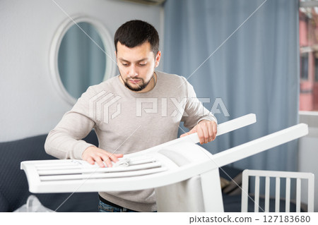 Smiling man wiping dust from a chair in room 127183680