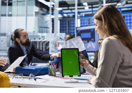 Investors review documentation on mockup device to evaluate investment profitability. Shareholders and production plant manager analyzing sustainable manufacturing data using isolated screen tablet 127183807