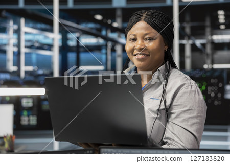 Portrait of smiling data center software developer using artificial intelligence neural networks. Cheerful server farm worker uses AI programming language on computer, configuring specialized hardware 127183820
