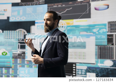 Male entrepreneur taking a phone call to share insight on KPI metrics and evaluate company performance. Specialist using remote communication to improve his profitability, greatness. 127183834