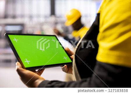 Manufacturing engineer presenting a tablet with isolated copyspace in industrial workspace. Selective focus of device displaying blank chromakey screen held by smart factory employee. 127183838