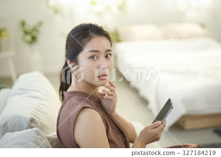 一位二十多歲的女性坐在沙發上操作智慧型手機 127184219