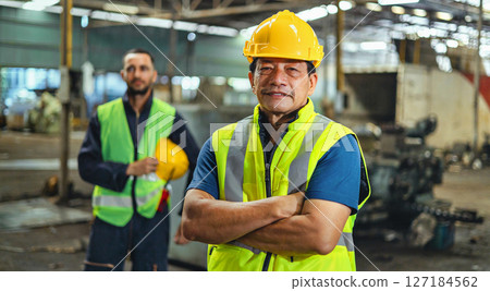 Two men wearing safety gear and yellow helmets stand in front of a building 127184562