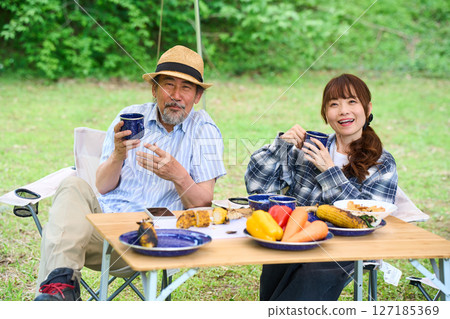 Mature couple camping outdoors barbecue BBQ family colleagues friends Mature couple camping outdoors barbecue BBQ family colleagues friends 127185369
