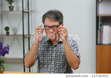 Senior man eye strain after for long stretches at computer or digital screens. Senior man eye strain after for long stretches at computer or digital screens. 127185443