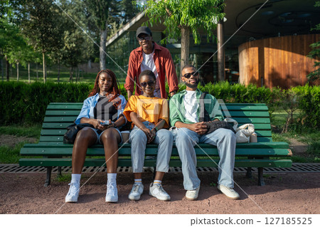 Happy young couples, black men and women, sit on park bench during double date, looking at camera 127185525