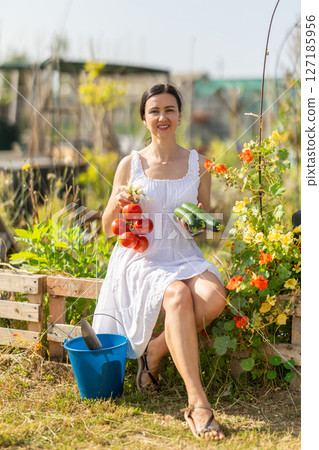 Woman in white dress with ripe vegetables in her hands - tomatoes, zucchini and green onions 127185956