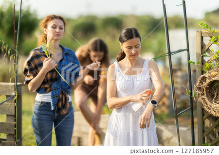 Three women applying repellent in cottage garden Three women applying repellent in cottage garden 127185957