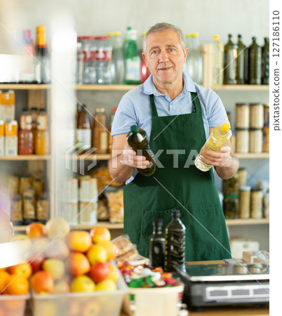 Senior man offers to buy vegetable oil, holds out bottles towards buyer, demonstrates best offers. Senior man offers to buy vegetable oil, holds out bottles towards buyer, demonstrates best offers. 127186110