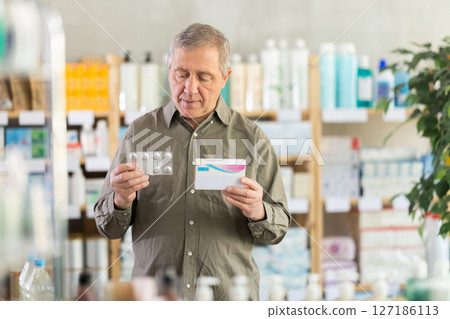 Senior man examining tablet blister and packaging at pharmacy 127186113