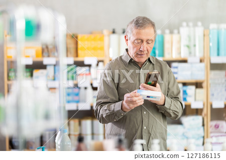 Senior man in pharmacy scans QR code on ointment for bruises 127186115