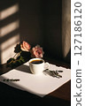 White coffee cup on blank paper, bathed in sunlight and shadows. Pink roses and lavender add beauty. Ideal for cozy, aesthetic, and peaceful morning. 127186120