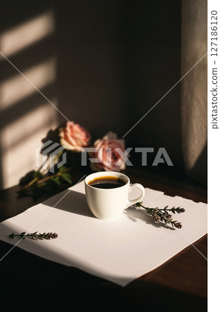 White coffee cup on blank paper, bathed in sunlight and shadows. Pink roses and lavender add beauty. Ideal for cozy, aesthetic, and peaceful morning. White coffee cup on blank paper, bathed in sunlight and shadows. Pink roses and lavender add beauty. Ideal for cozy, aesthetic, and peaceful morning. 127186120