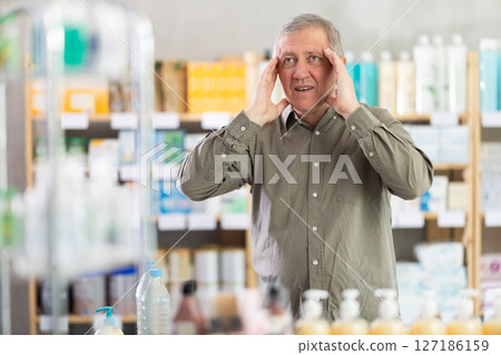 Senior man with headache looking for medicine in pharmacy 127186159